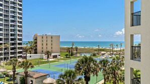 A resort with a tennis court, palm trees, and a view of the beach and ocean.