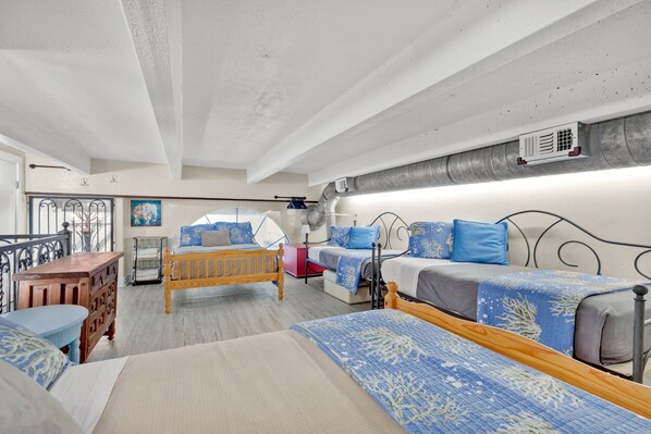A bedroom with two beds, a wooden dresser, a small table, and a balcony with a railing.