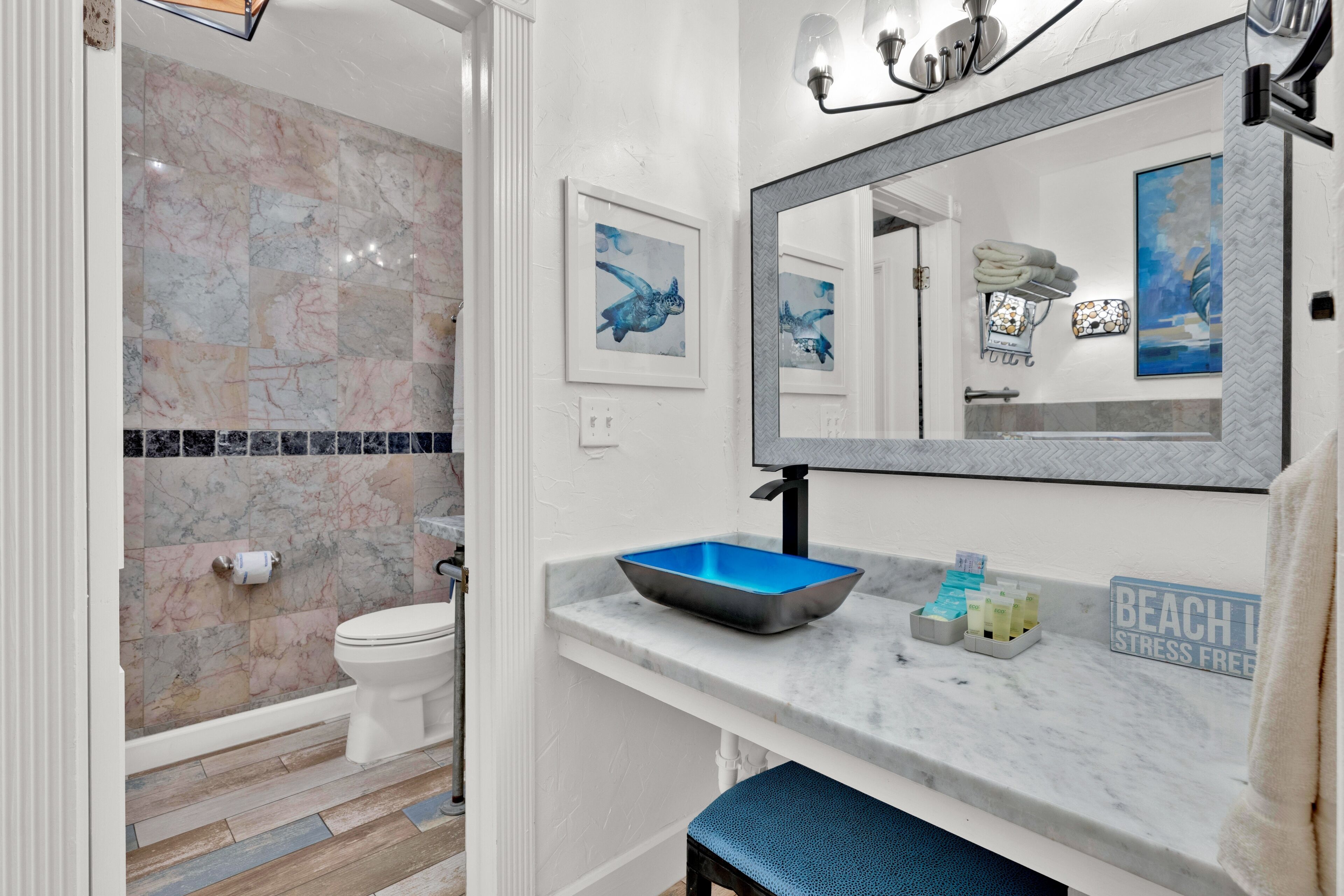 A bathroom with a marble wall, a sink with a blue basin, a mirror, and a towel rack.
