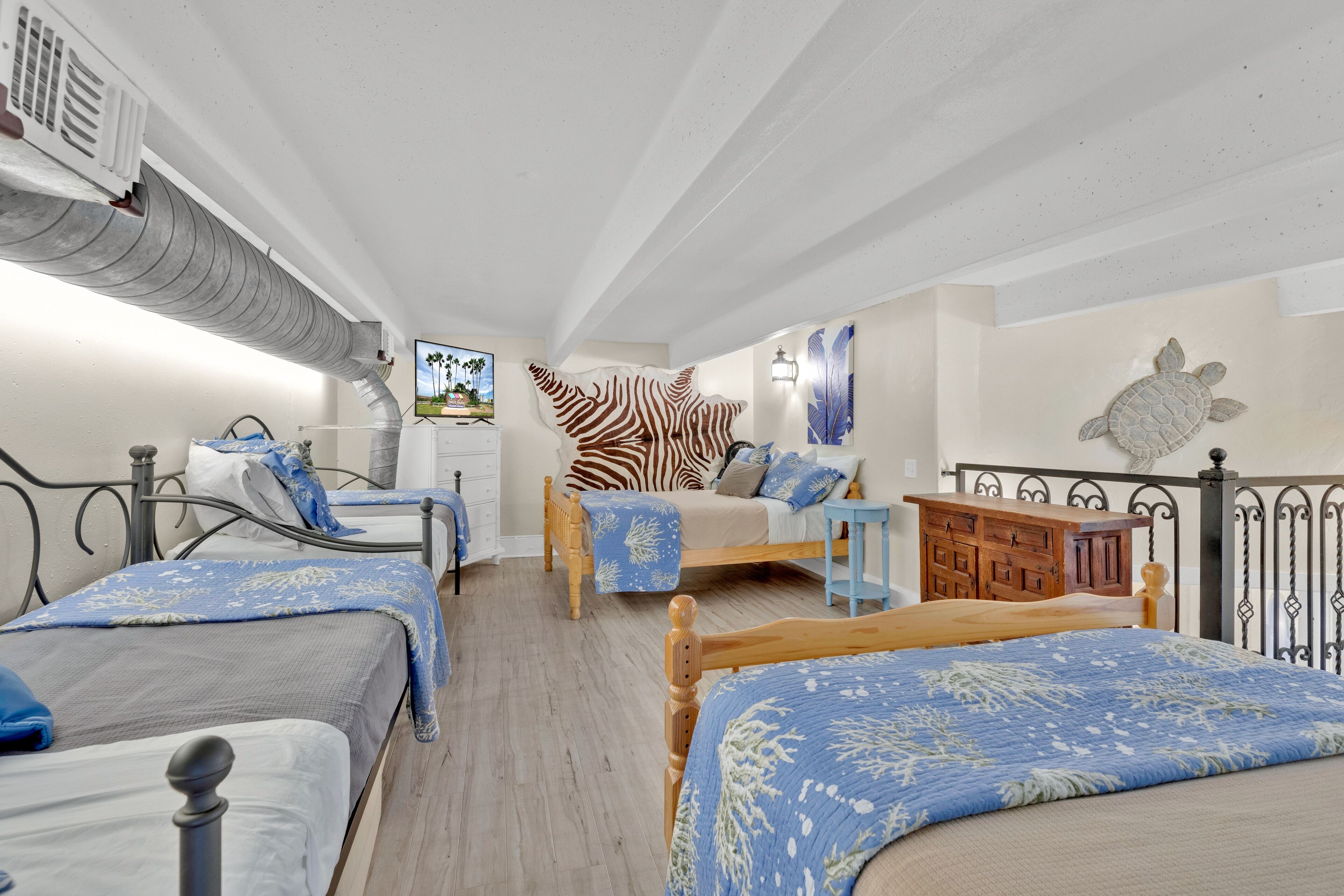A bedroom with two beds, a zebra-themed wall hanging, a turtle wall decoration, and a wooden cabinet.