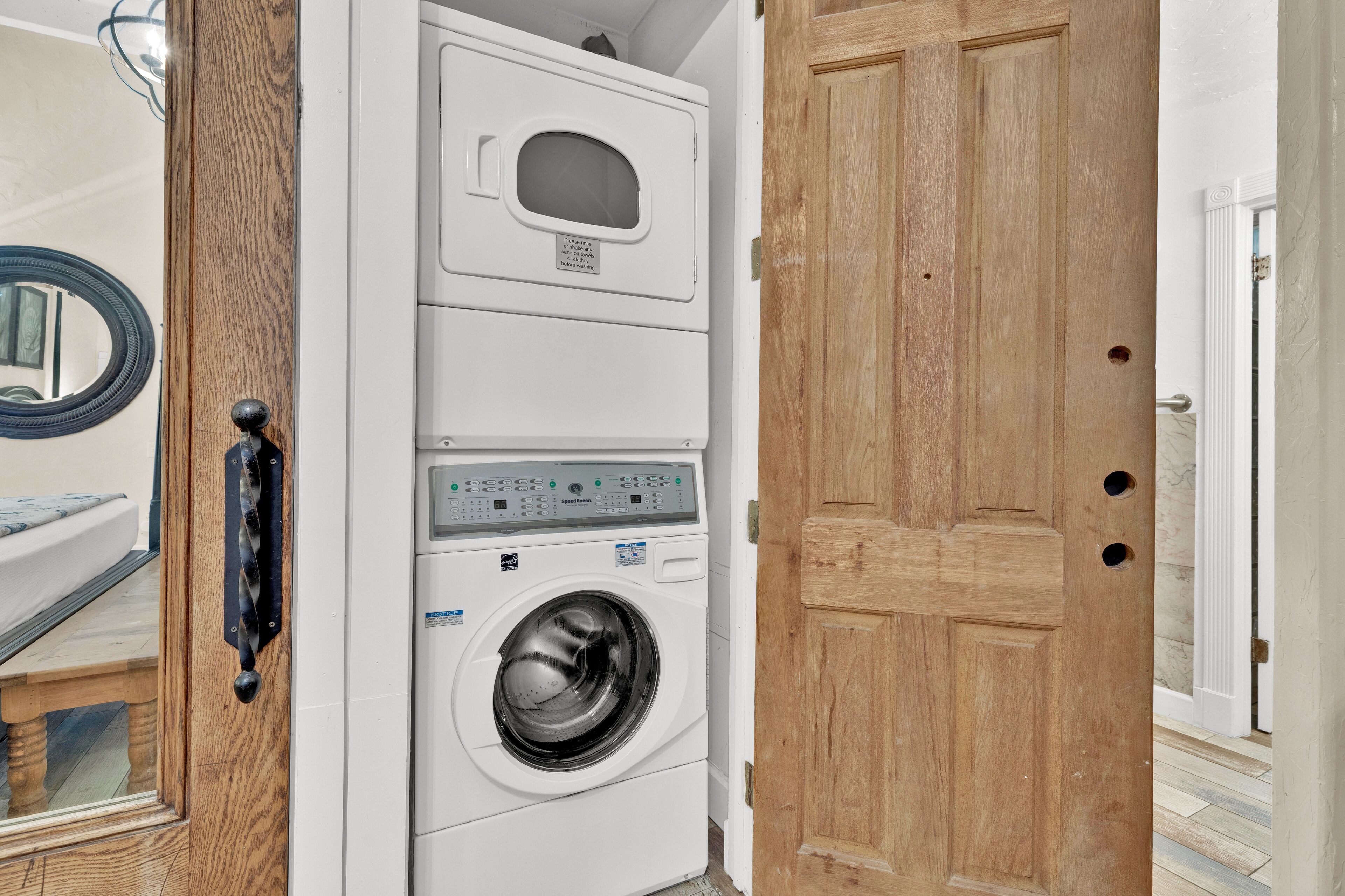 Une machine à laver et un sèche-linge superposés dans une pièce dotée d’une porte en bois et d’un miroir au mur.