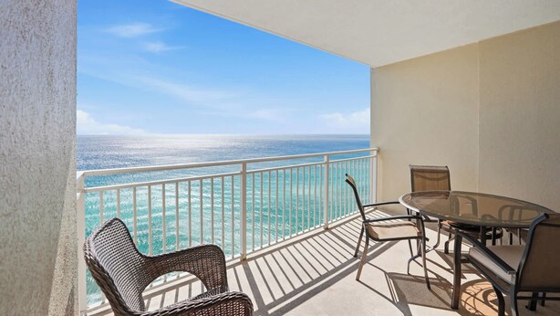 A balcony with a view of the ocean, a table with chairs, and a small table.