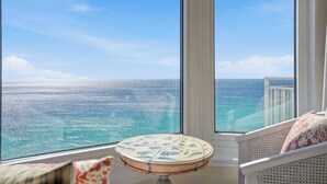 A balcony with a view of the ocean, a round table, and a white chair.