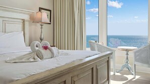 A hotel room with a bed, a lamp, a chair, and a view of the ocean.