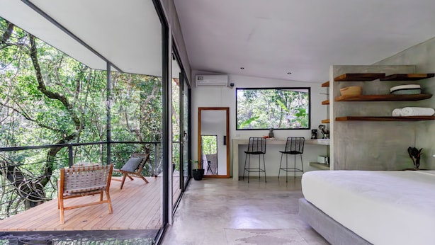 A modern bedroom with a large window, a balcony with a wooden deck, and built-in shelves.
