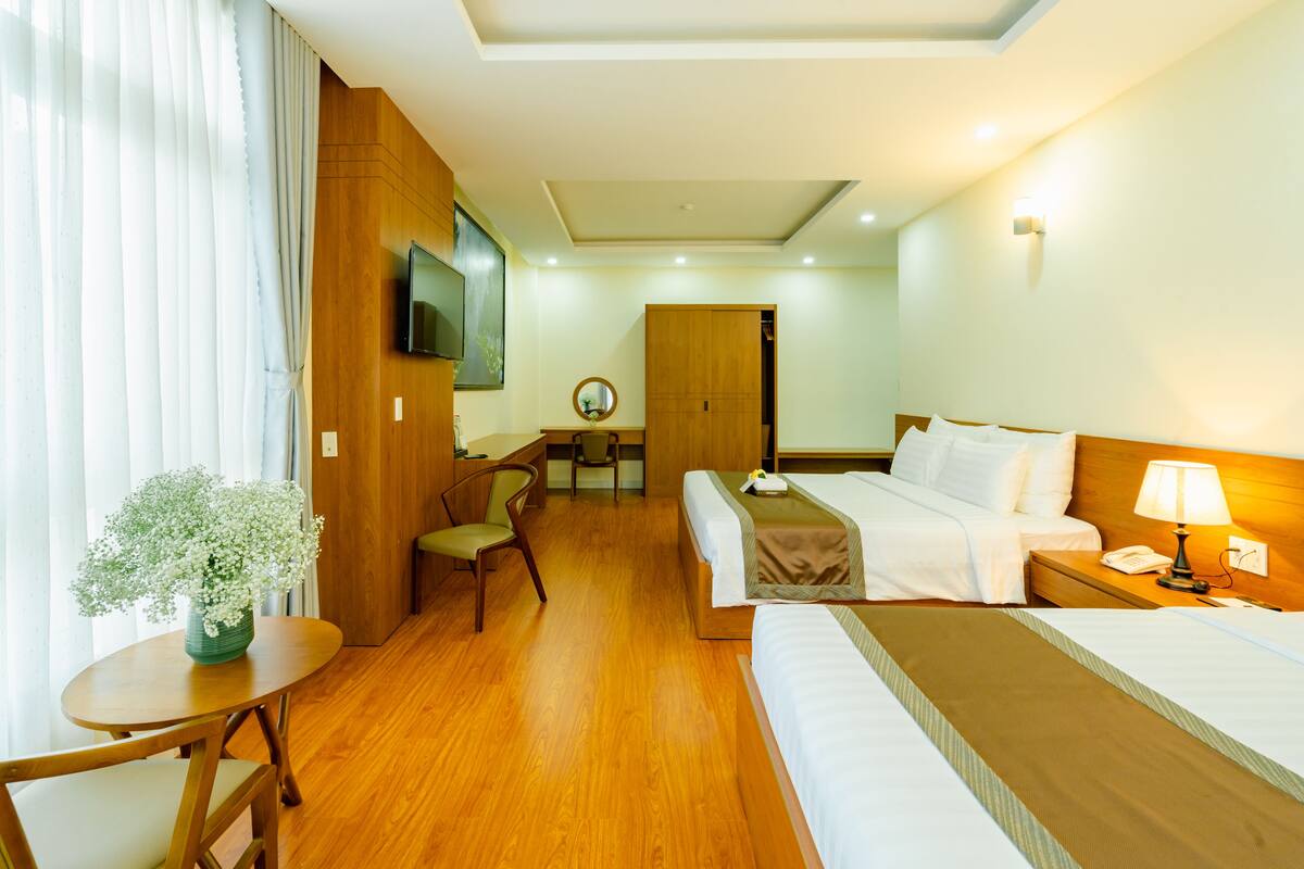 Une chambre d’hôtel avec un lit, une table de chevet, une lampe et une petite table sur laquelle est posé un vase de fleurs.