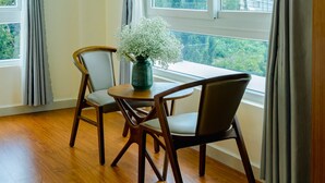 Una habitación con una mesa de comedor y sillas, un florero con flores, y vistas a edificios a través de amplios ventanales.