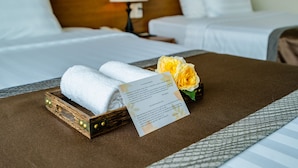 Una cama bien hecha con ropa de cama blanca, una bandeja de madera con toallas y una nota sobre la cama.