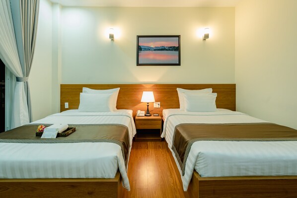 Habitación de hotel con dos camas, una mesita de noche con lámpara, un cuadro enmarcado en la pared y una ventana con cortinas.