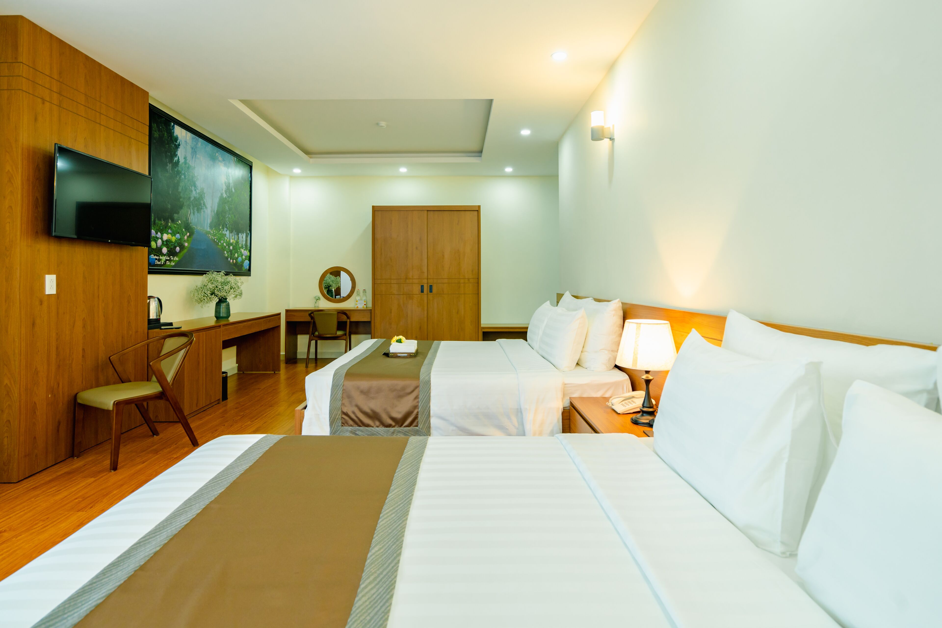 A hotel room with two beds, a desk, a chair, a TV, and a wooden wardrobe.