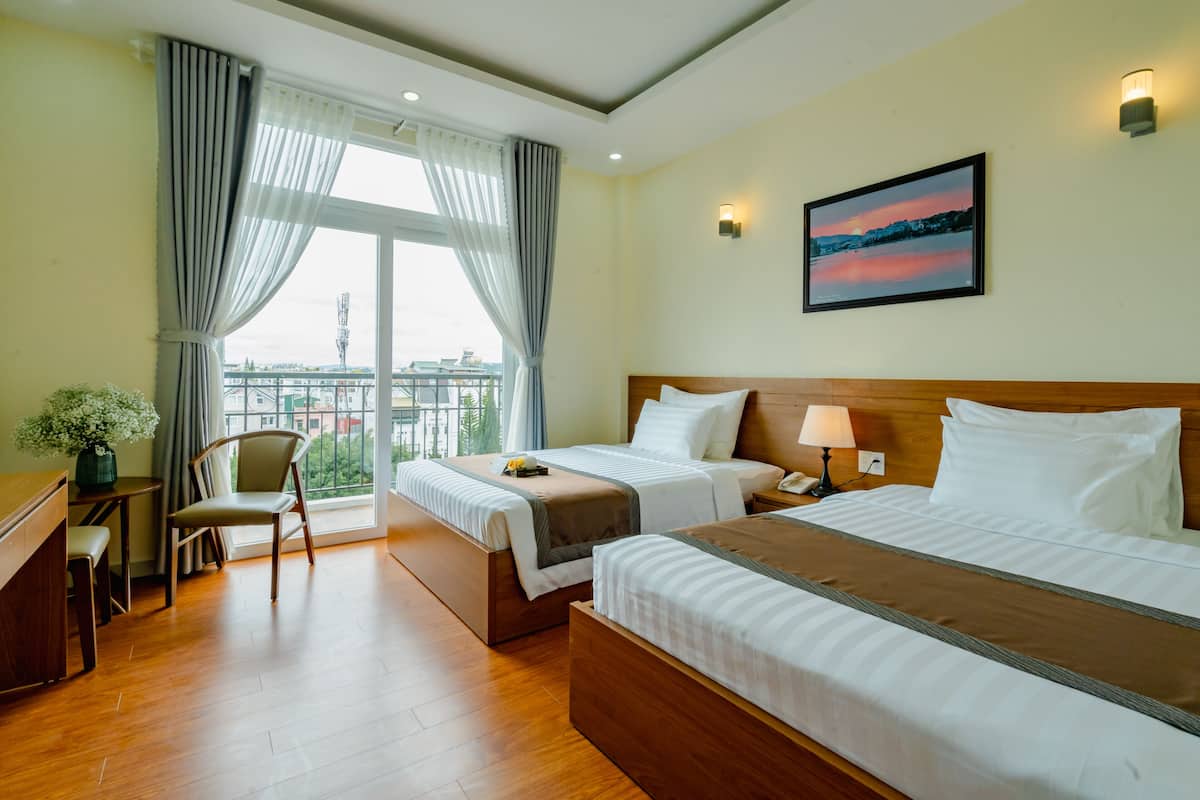 Une chambre d’hôtel avec deux lits, un bureau, une chaise et une grande fenêtre avec des rideaux.