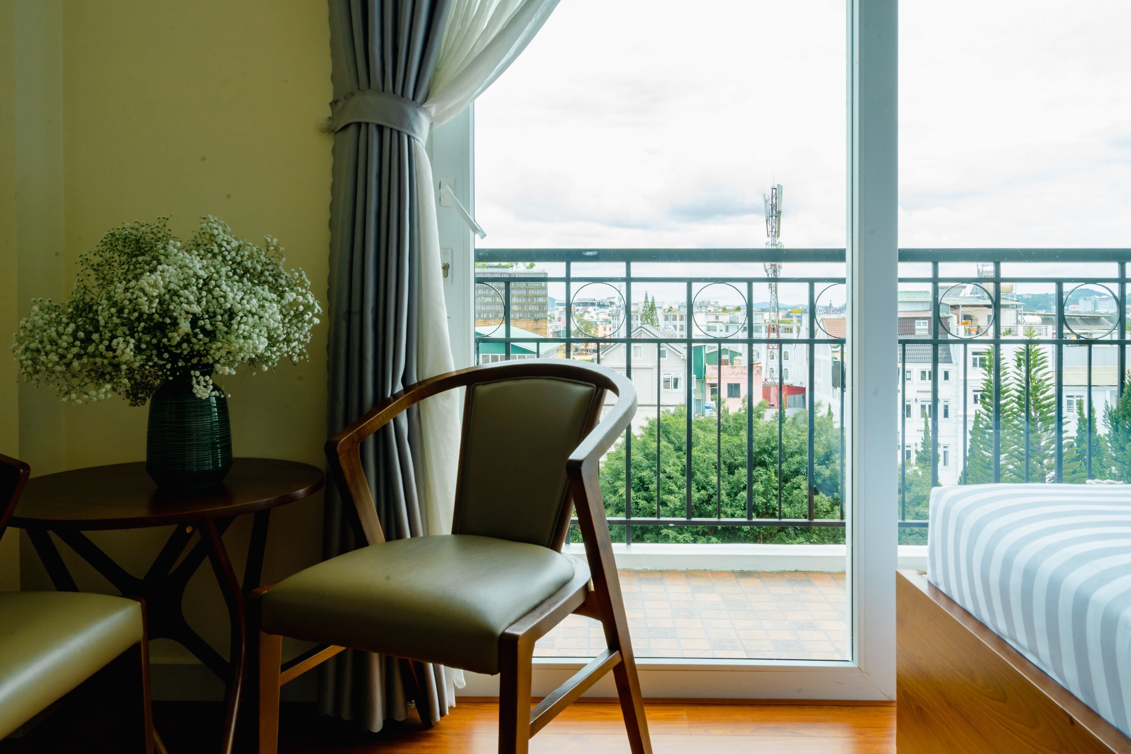Una habitación con vistas a la ciudad, una cama, una silla, una mesa y un florero con flores.
