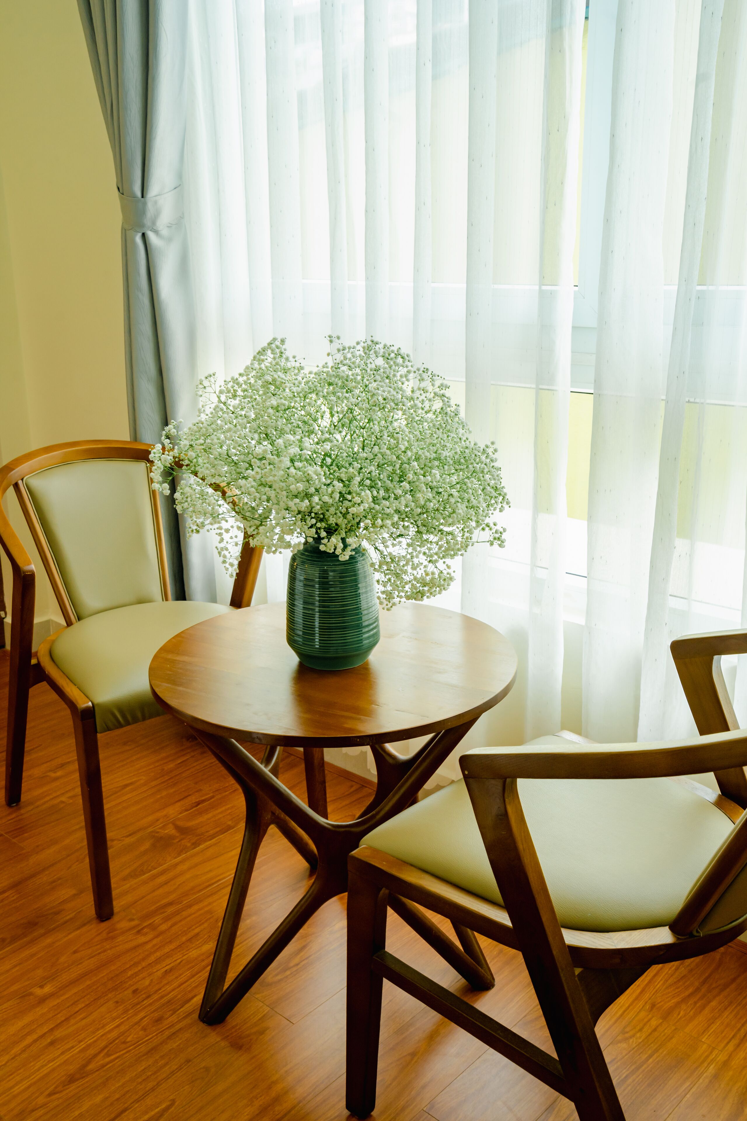 Een eetgedeelte met een ronde houten tafel, twee stoelen en een vaas met witte bloemen.