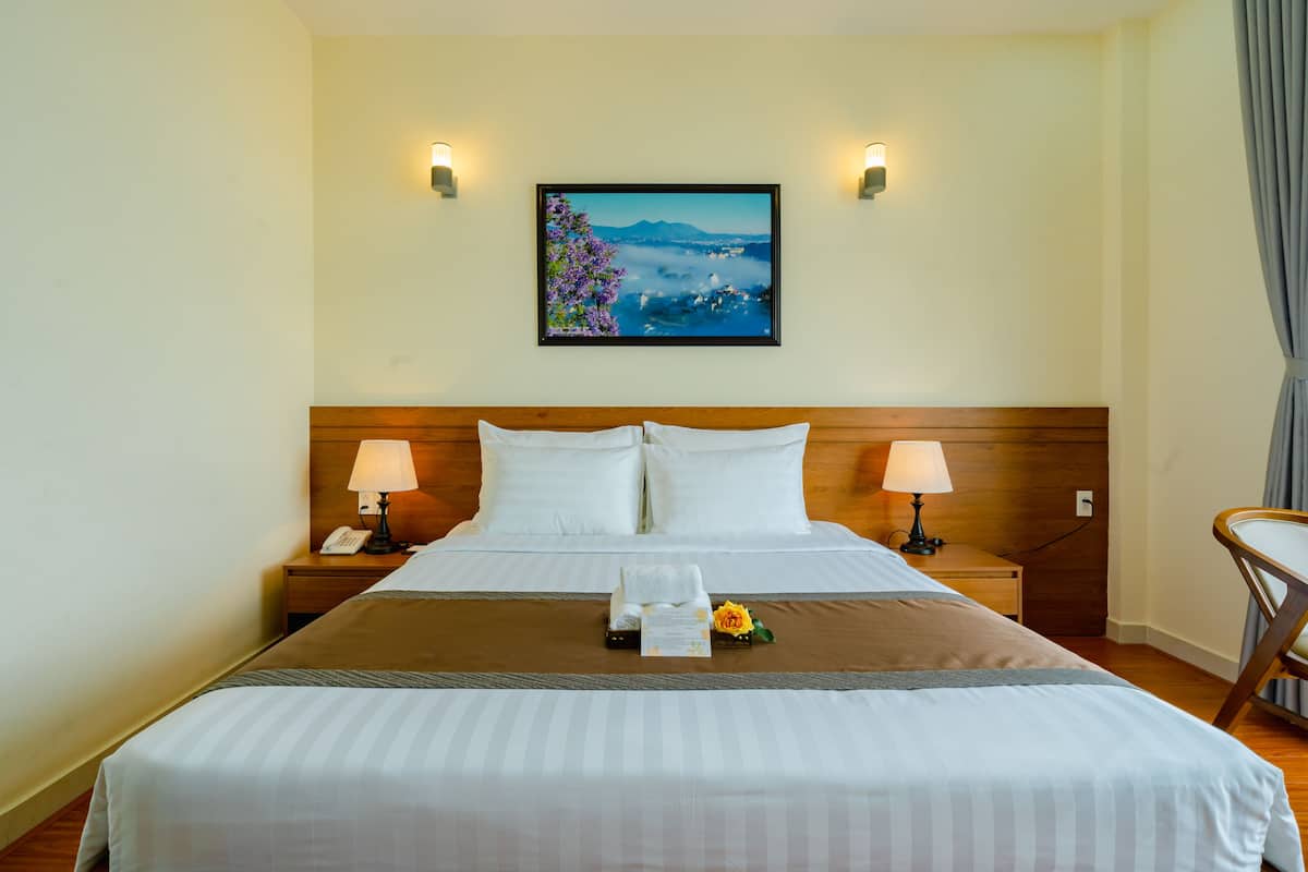 Une chambre d’hôtel avec un grand lit, deux lampes de chevet, un tableau encadré au mur et une tête de lit en bois.