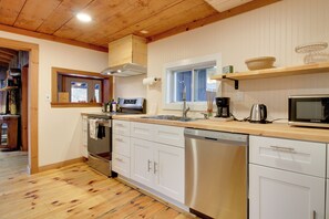 Uma cozinha moderna com piso de madeira, armários brancos, lava-louças de aço inoxidável e forno embutido.