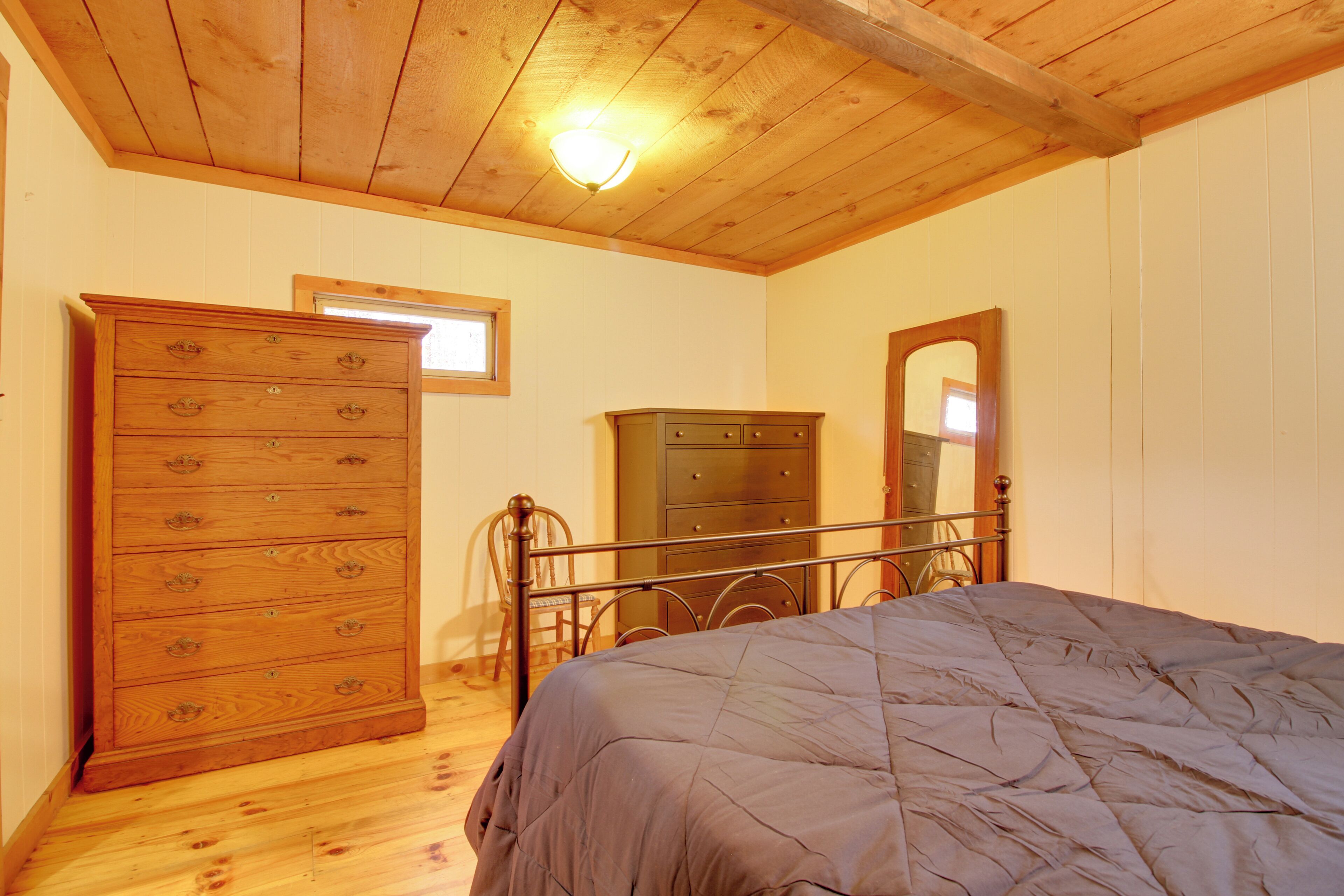 A bedroom with a wooden ceiling, a bed with a quilt, a dresser, and a mirror.