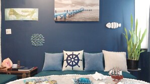 A bedroom with a bed, pillows, a map, a ship wheel pillow, a ship model, and a plant.