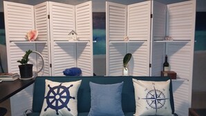 A room with a teal sofa, three white louvered partitions, and various decorative items including a potted plant, a blue bottle, and a wine bottle.