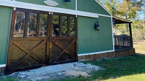 A green barn with a large wooden door, a window, and a 'Welcome to the Farm' sign. - Barn Loft on Gated Horse Farm (Greenville)