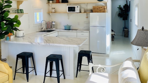 A modern kitchen with wooden ceiling, white cabinets, a central island with stools, and a dining area with a sofa and table. - Barn Loft on Gated Horse Farm (Greenville)