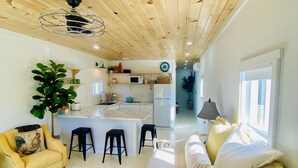 A modern kitchen with a central island, a dining area with stools, a sofa, and a large plant. - Barn Loft on Gated Horse Farm (Greenville)