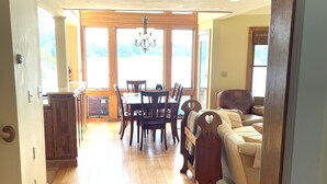 Un comedor espacioso con una mesa y sillas de madera, una araña y ventanas amplias que ofrecen vistas al exterior.