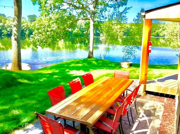 Une table en bois, des chaises rouges, un espace verdoyant et une vue sur un lac.
