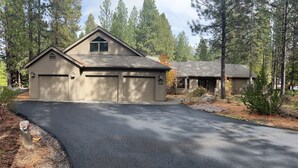 A two-story house with a garage, surrounded by trees and a paved driveway. - Big, Beautiful Golf Home, sleeps 14, situated on the golf course (Black Butte Ranch)
