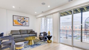 A spacious living room with a grey sofa, a round gold coffee table, and a large window offering a view of a building and street. - Capitol View 3 Penthouse with Rooftop (Washington)