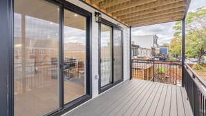 A covered deck with large sliding glass doors, wooden flooring, and a view of the surrounding neighborhood. - Capitol View 3 Penthouse with Rooftop (Washington)