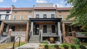 A multi-story residential building with a brick facade, a central entrance with a porch, and a stone retaining wall in front. - Capitol View 3 Penthouse with Rooftop (Washington)