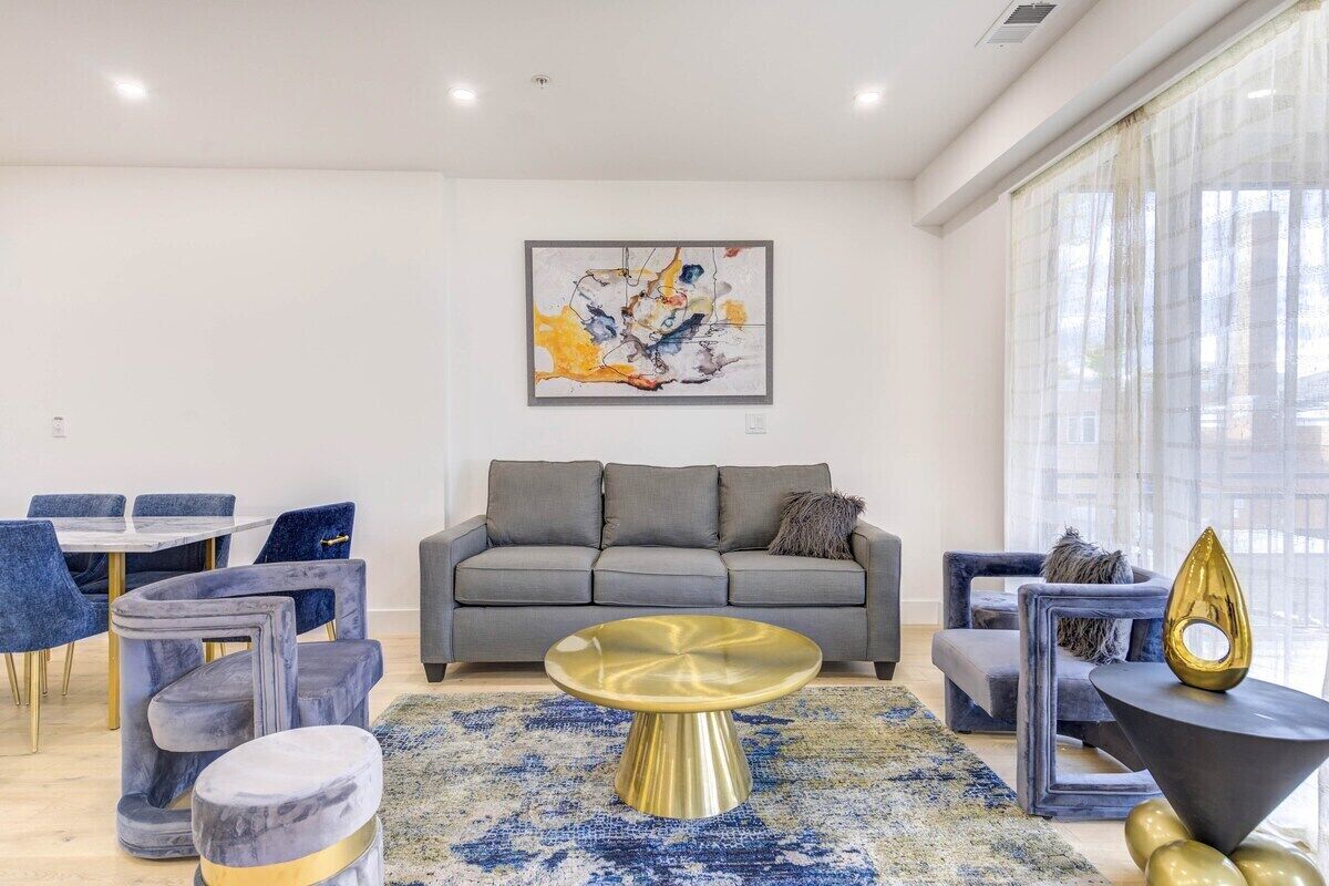 A modern living room with a grey sofa, a round gold coffee table, and a blue patterned rug.