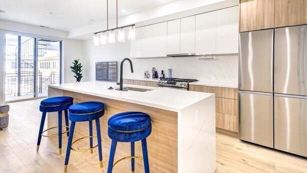 A modern kitchen with a large island, stainless steel appliances, and blue bar stools. - Capitol View 3 Penthouse with Rooftop (Washington)