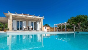 Ein Poolbereich mit überdachter Sitzecke, einem kleinen Gebäude und einer Pergola.