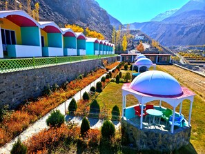A row of colorful, multi-story buildings with a stone retaining wall and a pathway lined with shrubs and flowers.