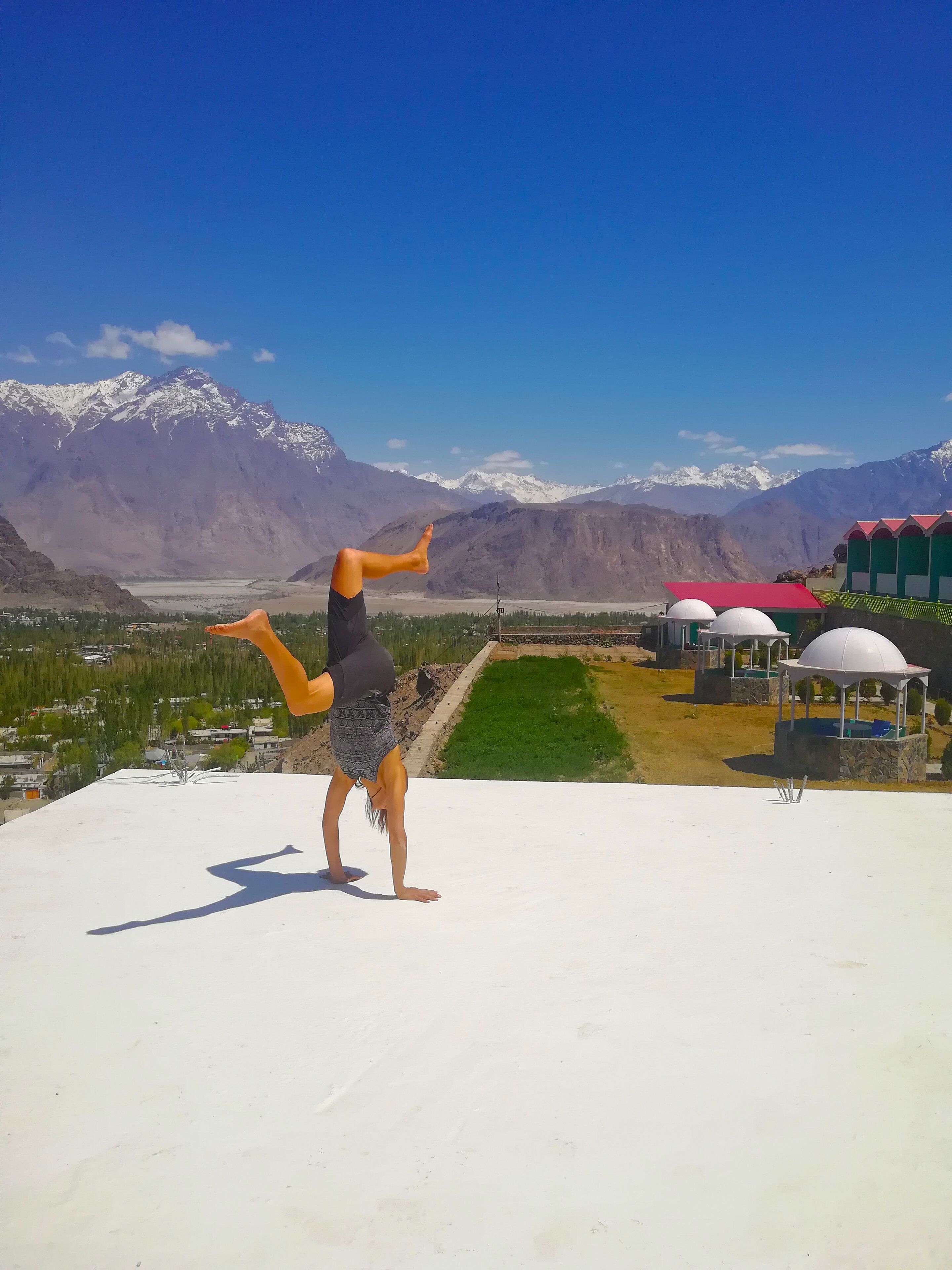 A person performing a yoga pose on a rooftop with a mountainous landscape in the background.