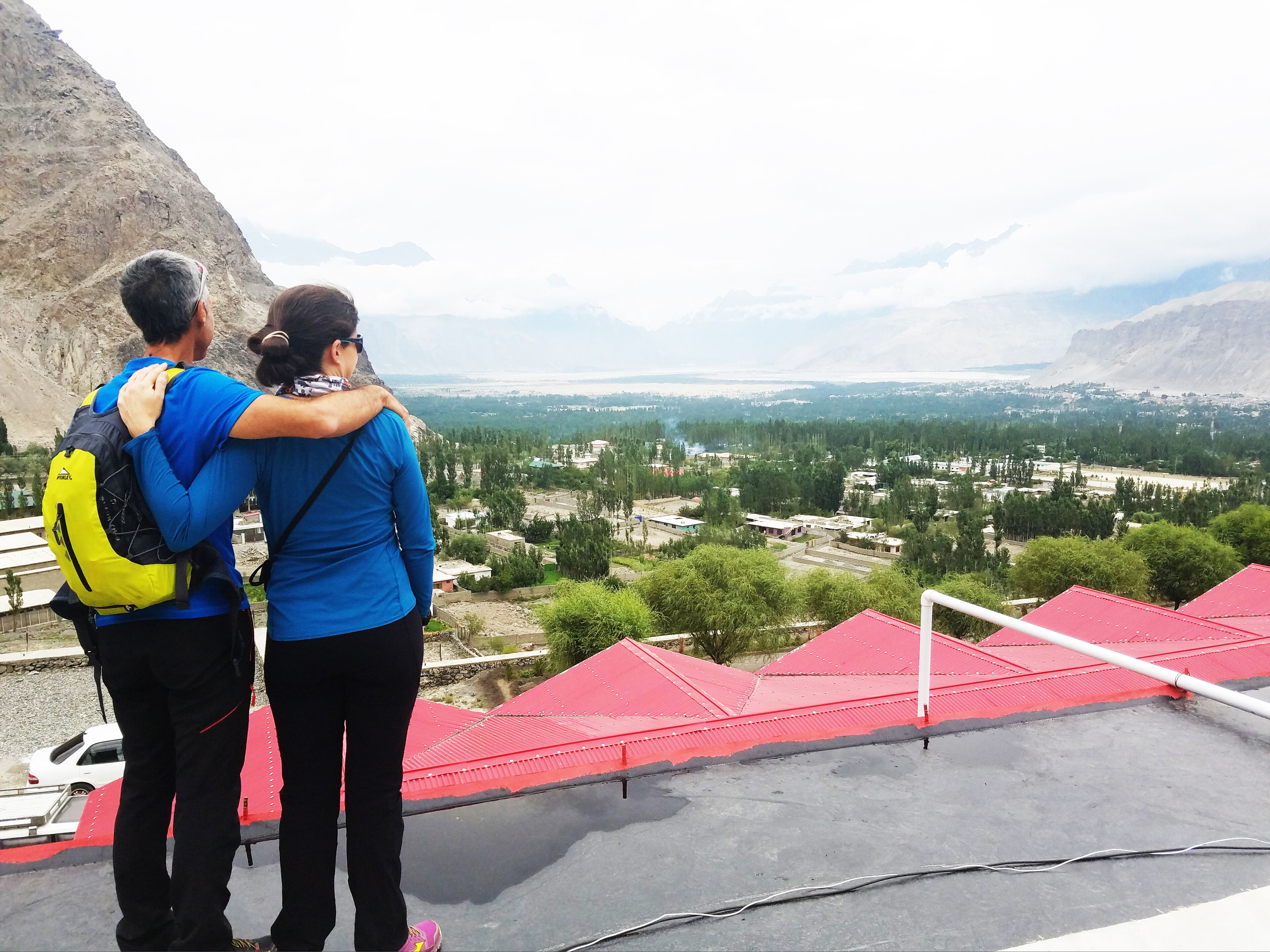 A couple standing on a rooftop with a view of a valley and mountains.