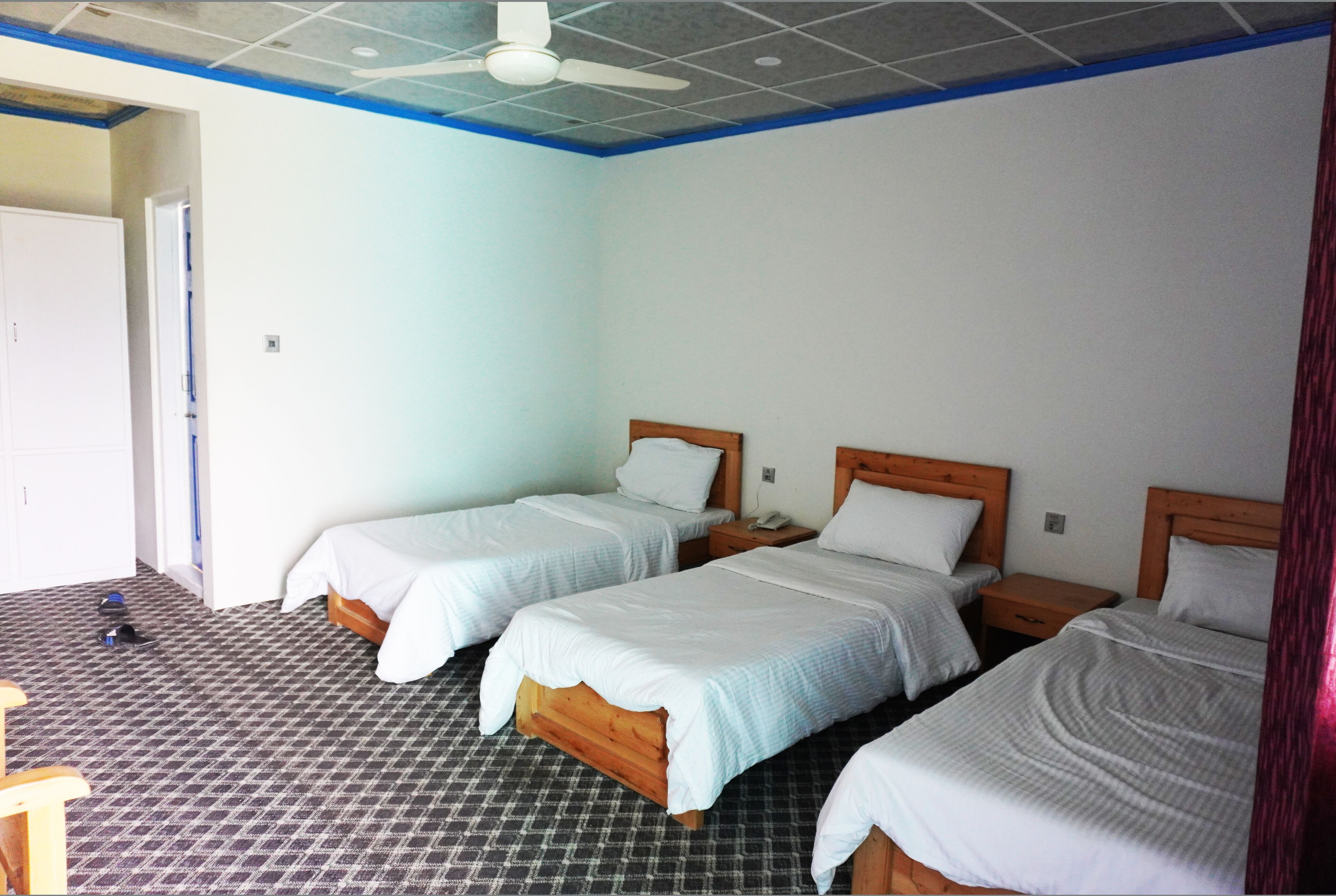 A room with three single beds, a ceiling fan, and a patterned floor.