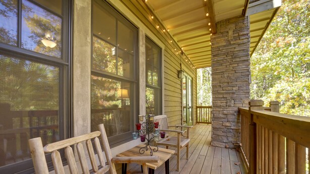 A wooden deck with benches and a table, large windows, and a stone pillar.
