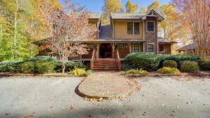A two-story house with a stone entryway, surrounded by autumn foliage and a clear sky.