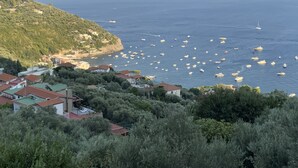 A coastal town with houses on a hillside overlooking the sea, boats anchored in the water, and a clear sky.