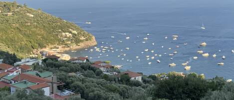 Un pueblo costero con casas en una colina con vistas al mar, barcos anclados en el agua y un cielo despejado.