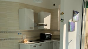 A compact kitchen with white cabinets, a microwave, and a glass table.