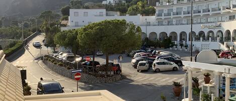 Vista de la calle con coches estacionados, un árbol y edificios, incluyendo un hotel con un letrero.