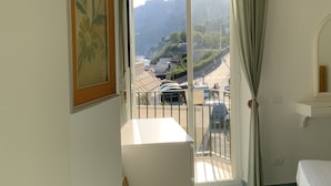 A room with a balcony, a bed, a chair, and a framed picture on the wall.