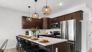 A modern kitchen with dark wood cabinets, stainless steel appliances, and pendant lighting. - Outdoor Theater, HotTub, Pool, Pickleball, Slps 24 (Kimberling City)