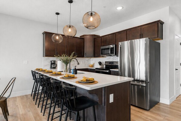 A modern kitchen with dark wood cabinets, stainless steel appliances, and pendant lighting.