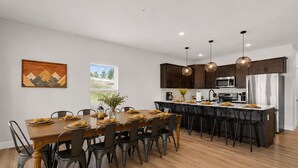 A modern kitchen with dark wooden cabinets, stainless steel appliances, and a dining area with a wooden table and chairs. - Outdoor Theater, HotTub, Pool, Pickleball, Slps 24 (Kimberling City)