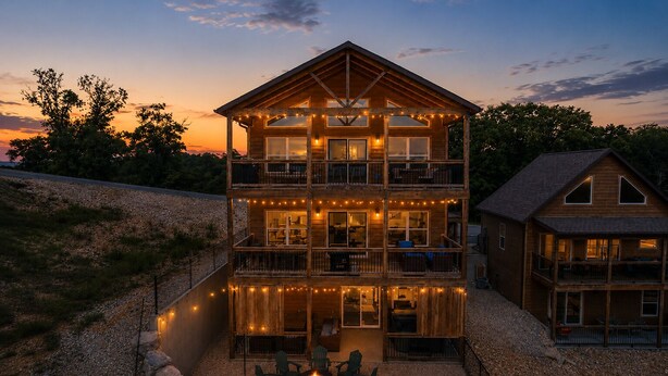 A multi-story wooden cabin with balconies, string lights, and a fire pit area. - Outdoor Theater, HotTub, Pool, Pickleball, Slps 24 (Kimberling City)