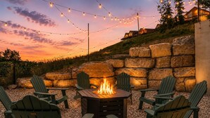 A fire pit with chairs around it, string lights overhead, and a stone wall in the background. - Outdoor Theater, HotTub, Pool, Pickleball, Slps 24 (Kimberling City)